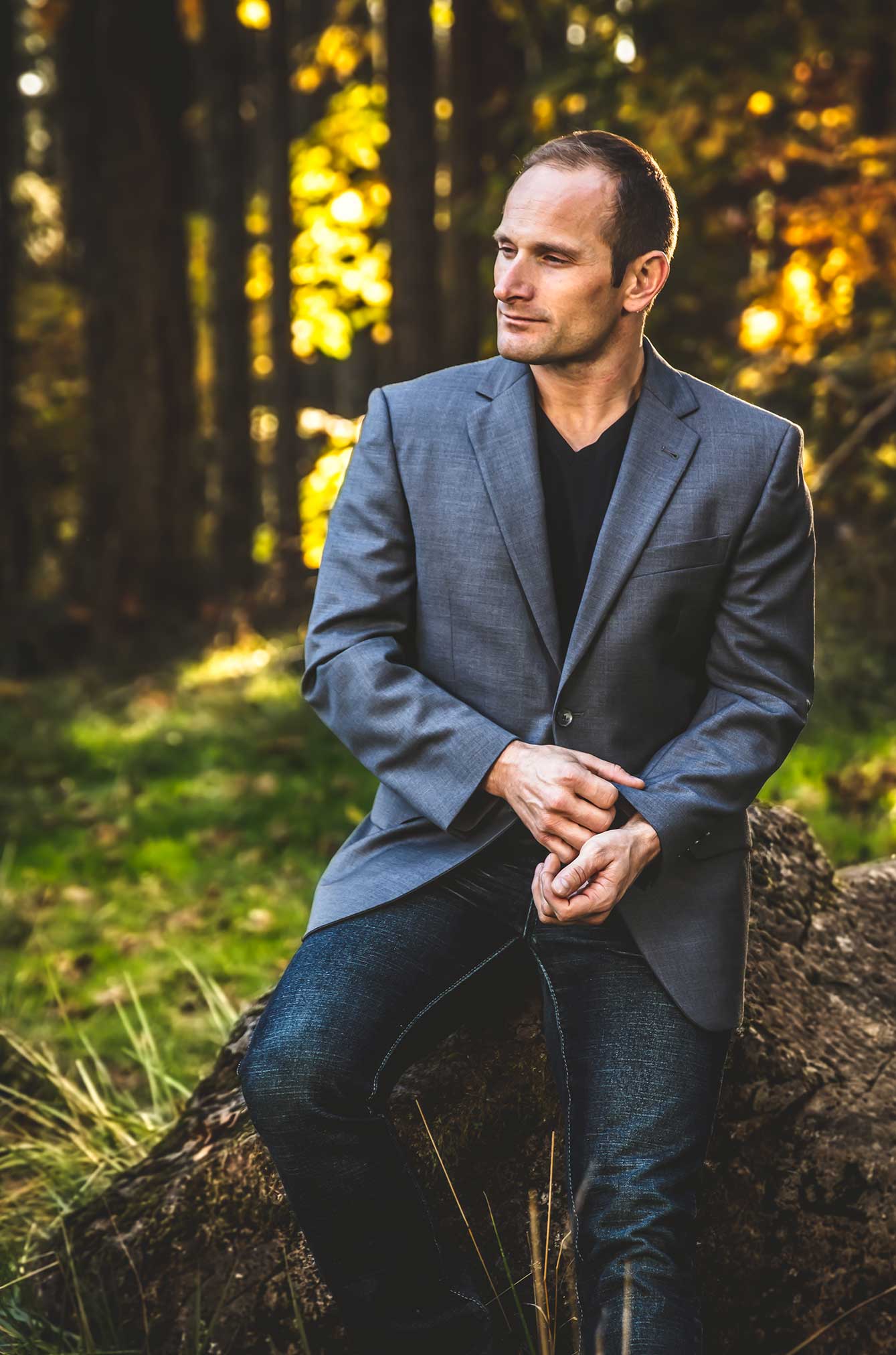 Man in blazer seated in sunlit forest
