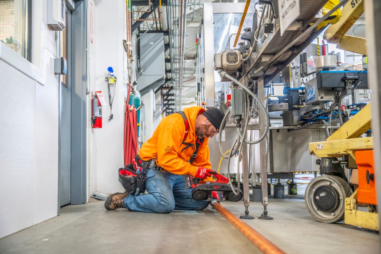 Plumber kneeling to cut pipe in brewery corridor