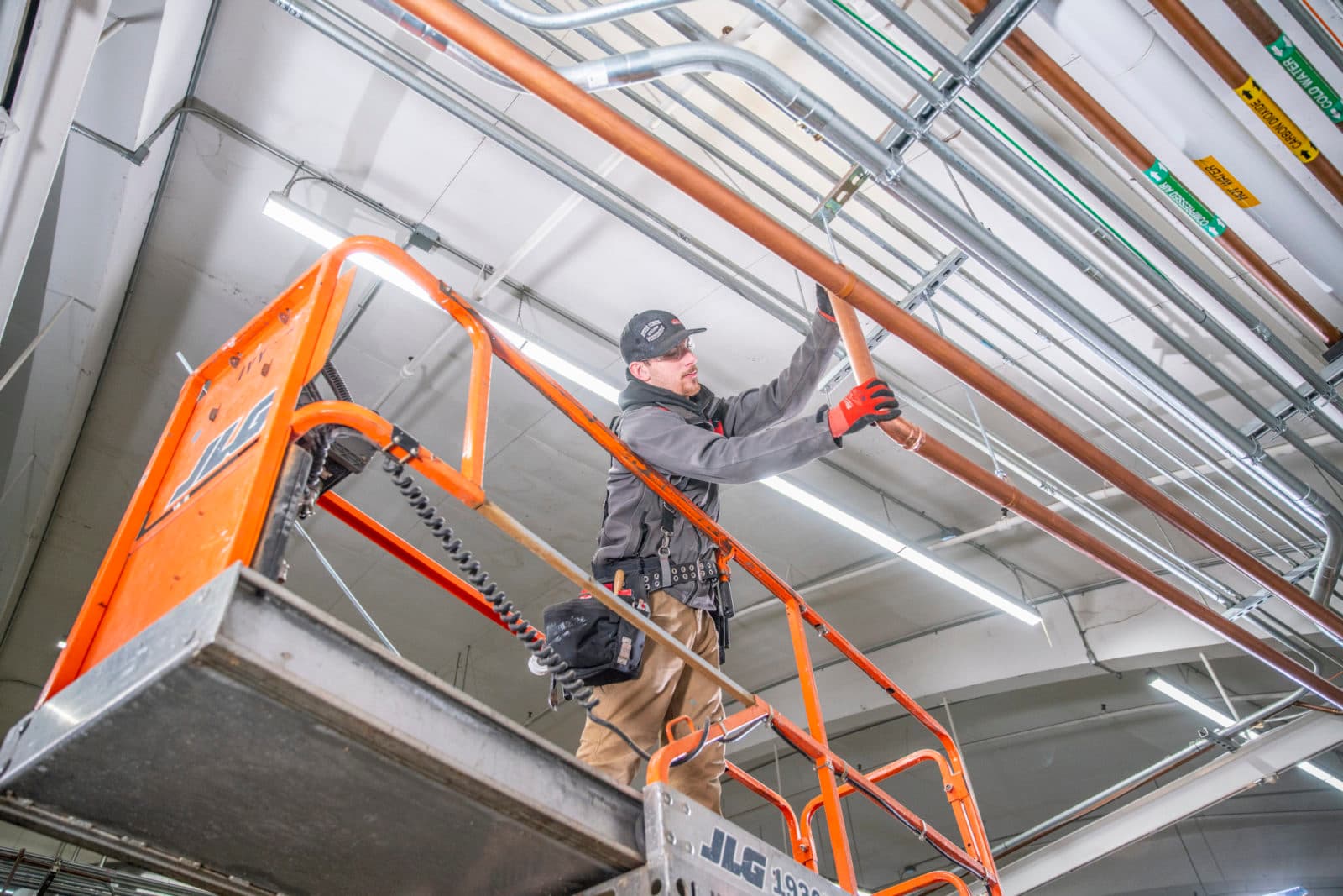 Plumber on scissor lift installing overhead pipe