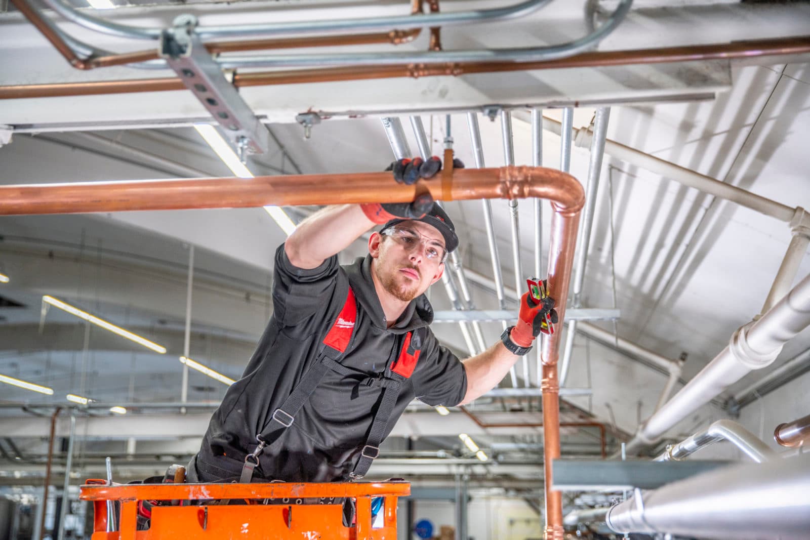 Plumber installing copper pipe from orange lift
