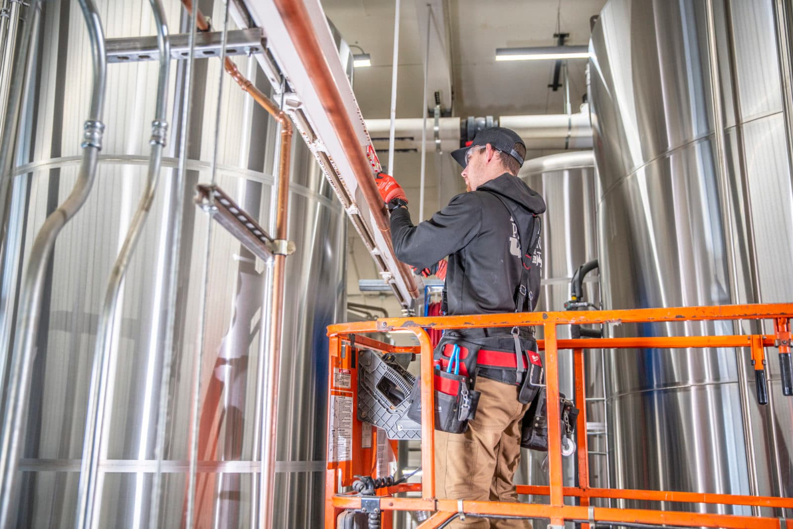 Plumber on lift among stainless tanks