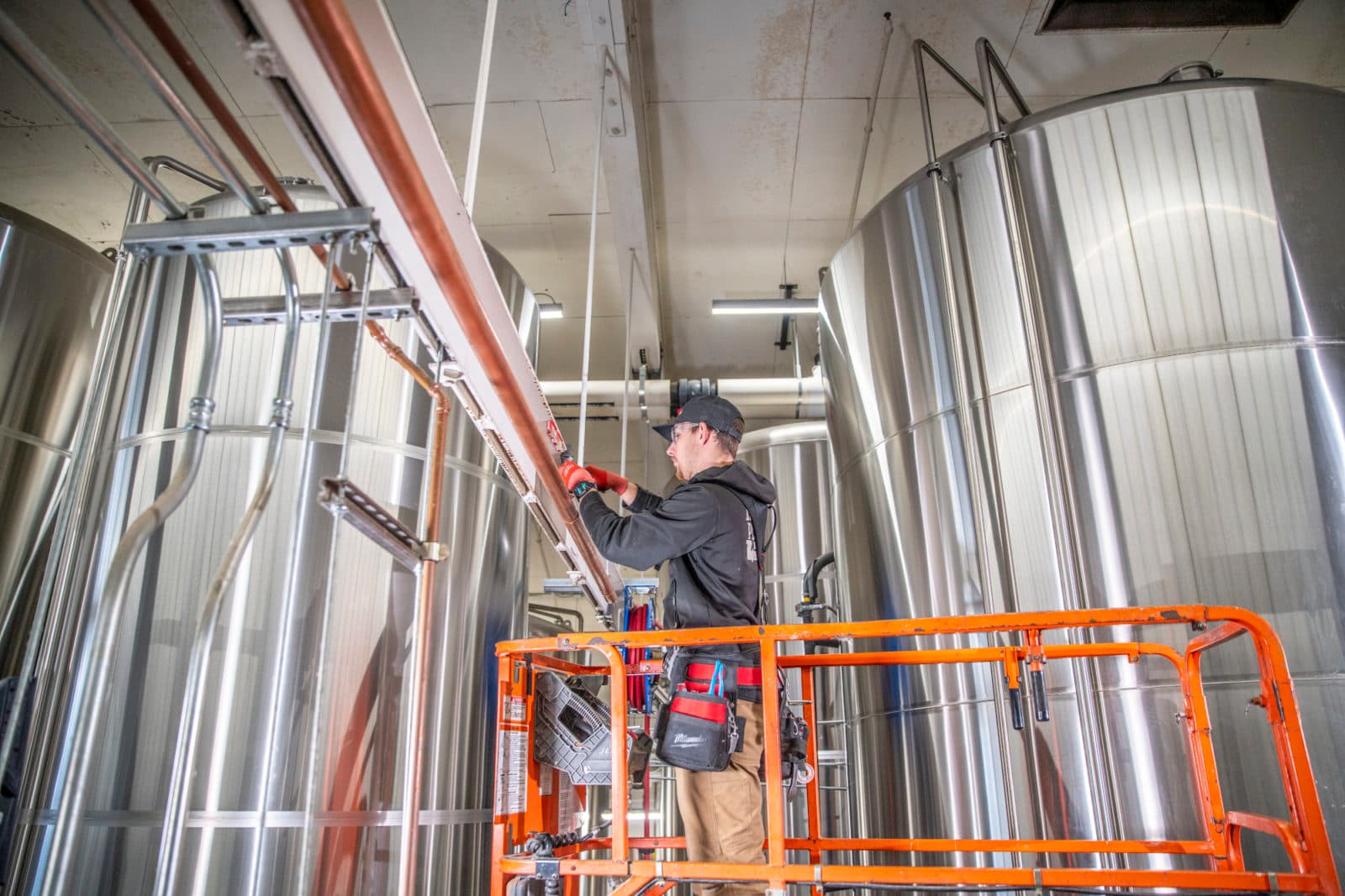 Plumber on scissor lift beside tall tanks