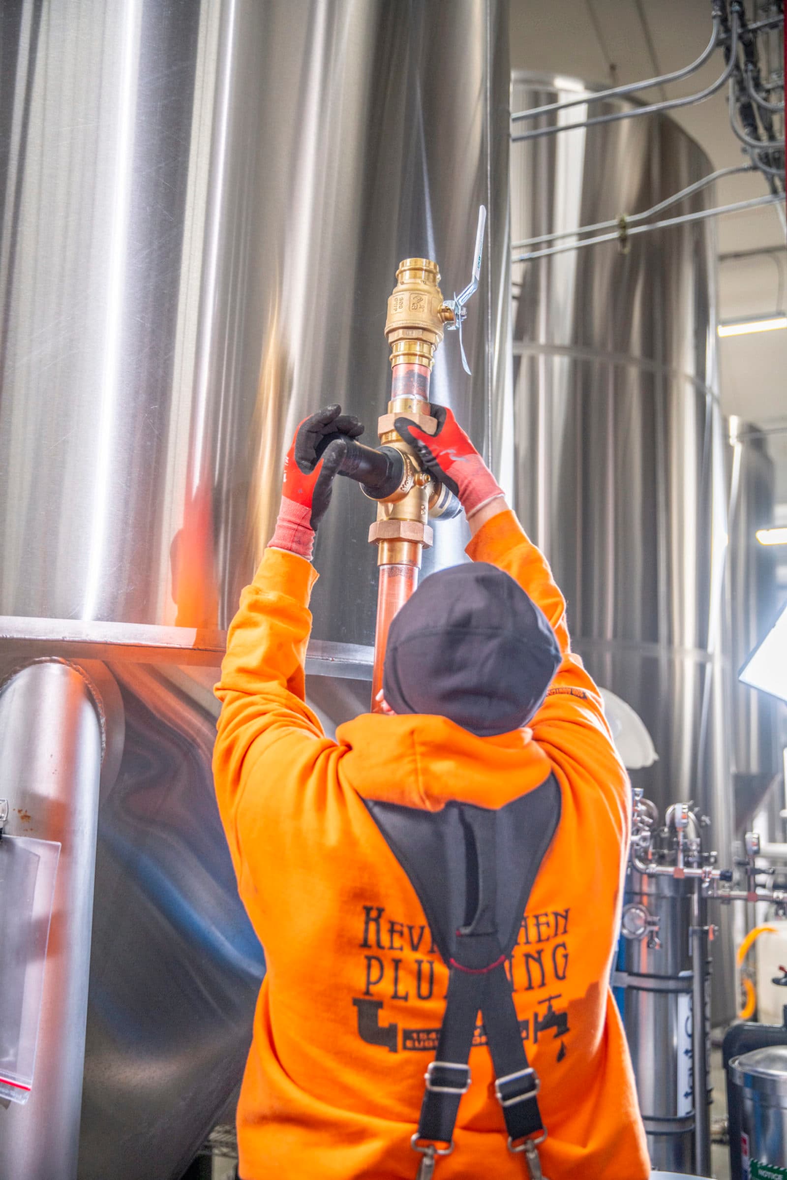 Plumber in orange hoodie at brass valve on tanks