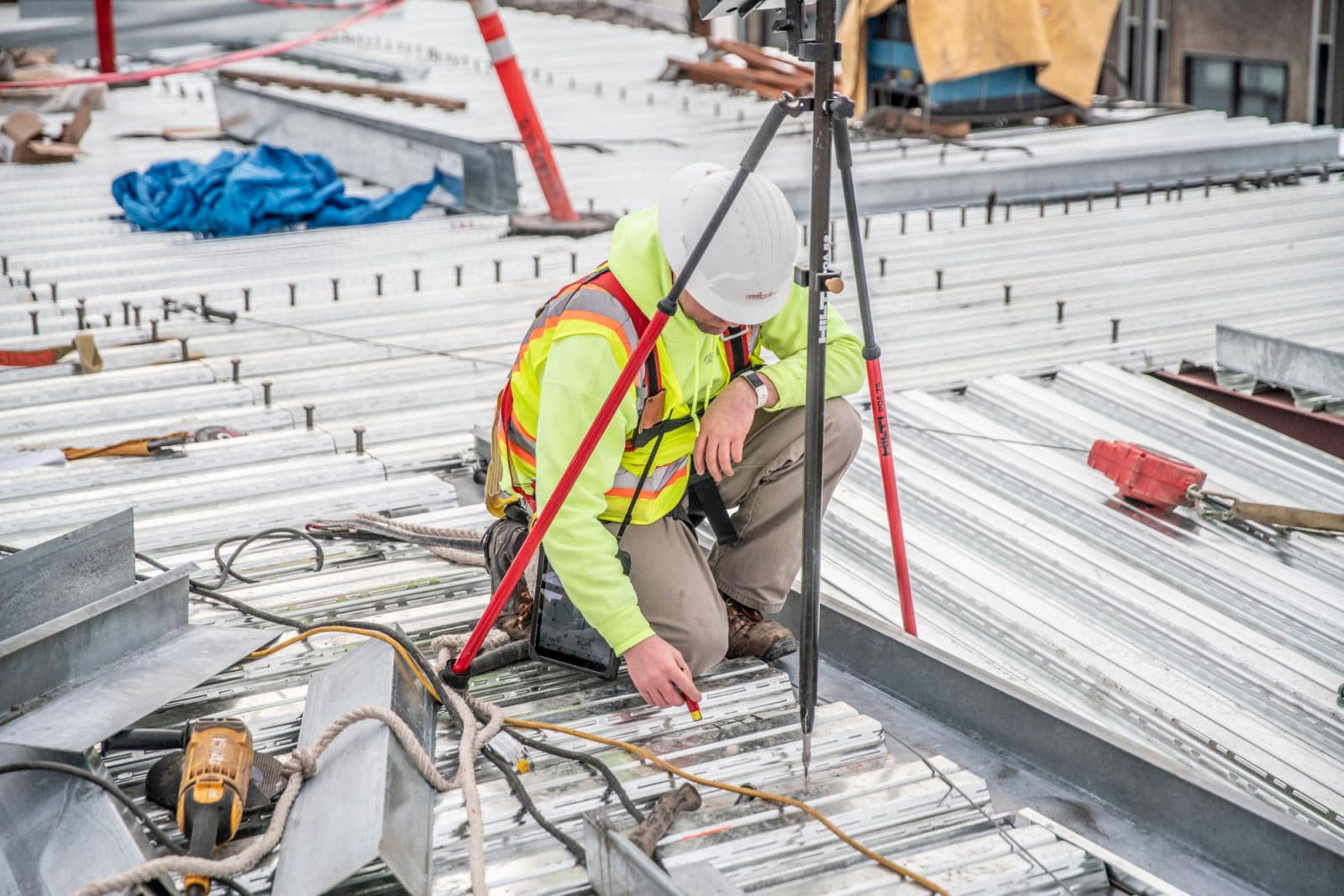 Worker crouching by tripod on metal roof