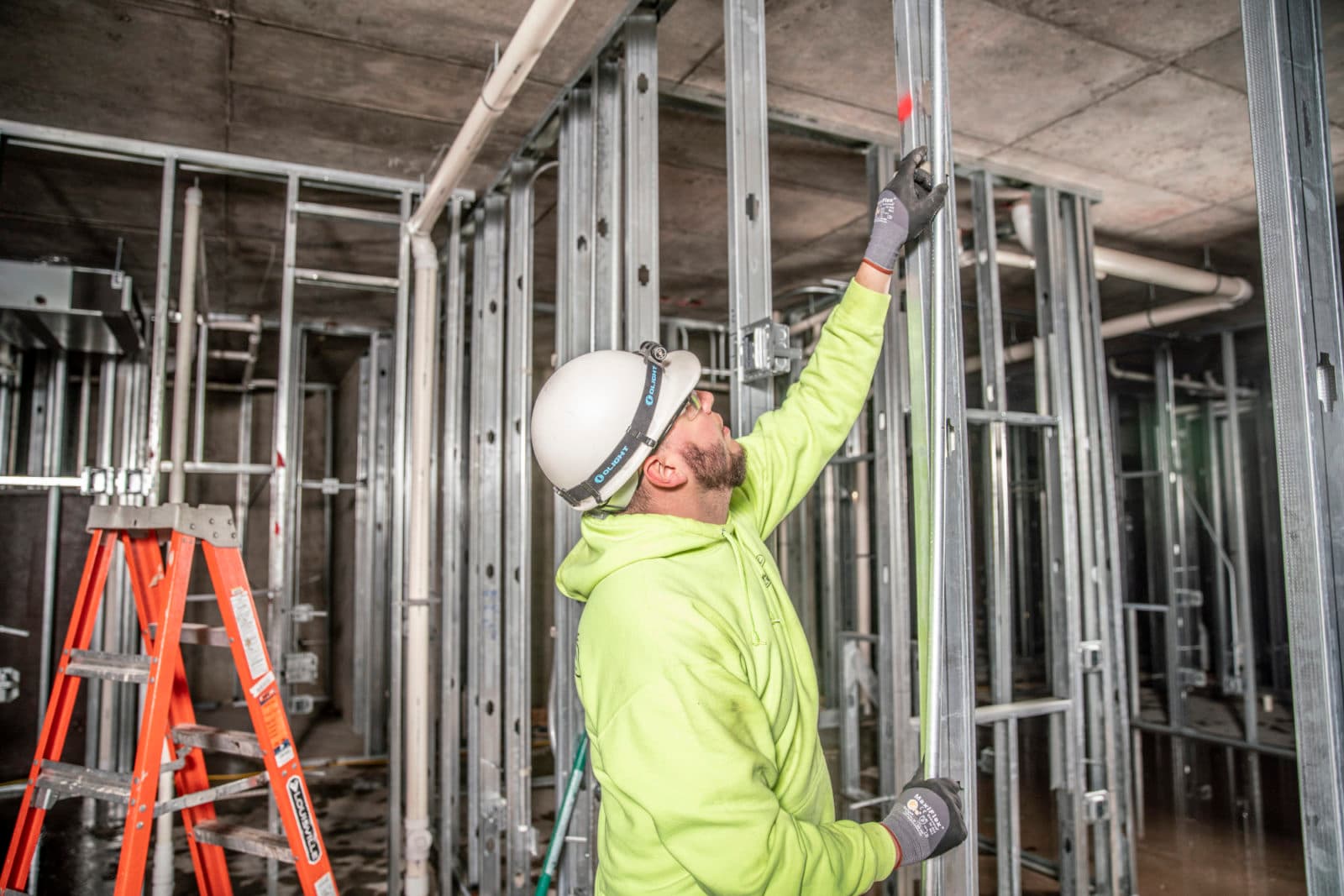 Electrician at metal-stud wall with orange ladder