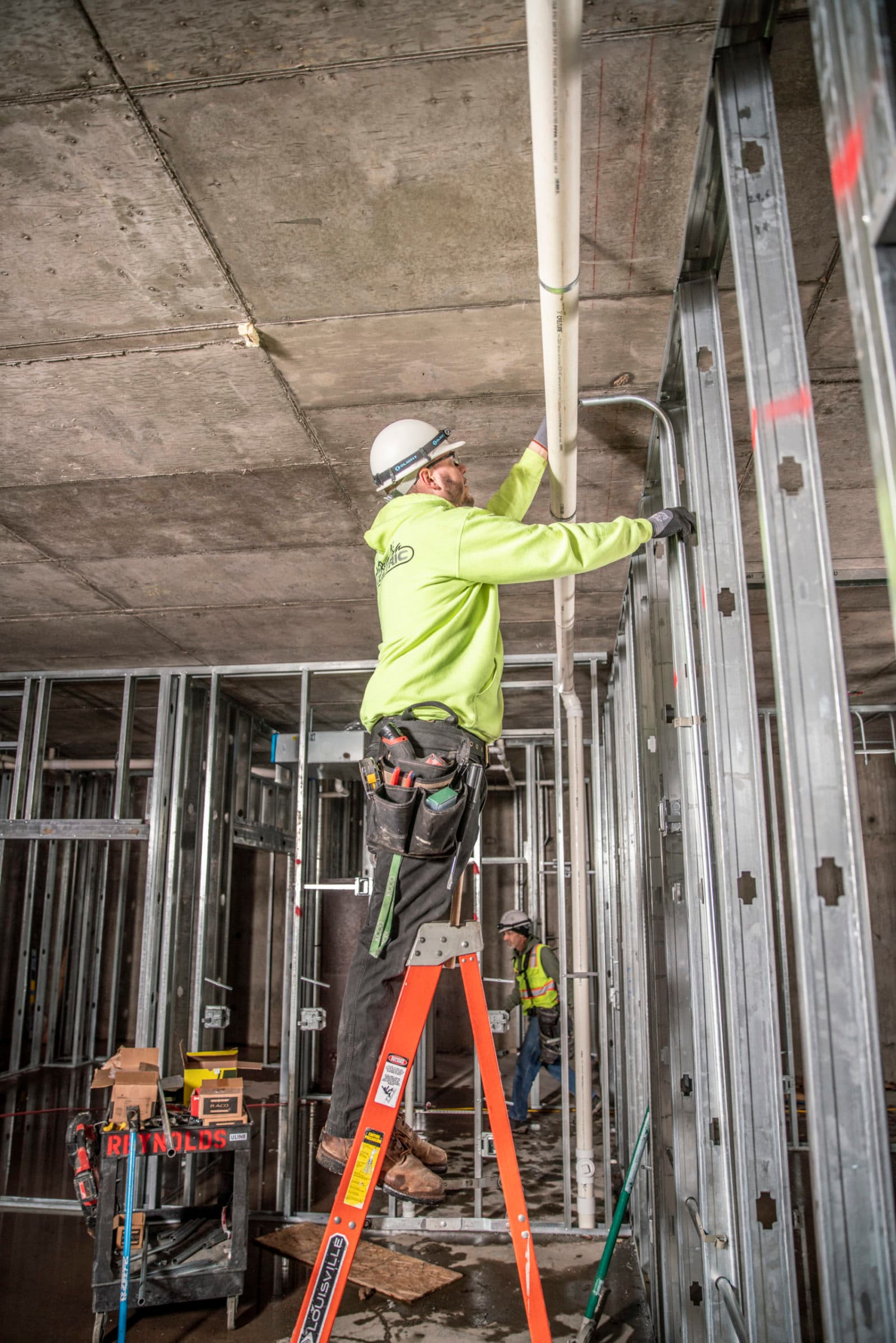 Electrician on ladder installing conduit (portrait)