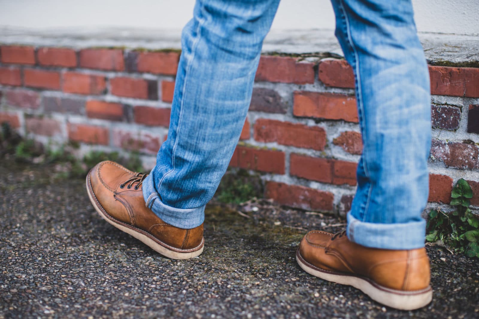 Walking feet in brown boots by brick wall