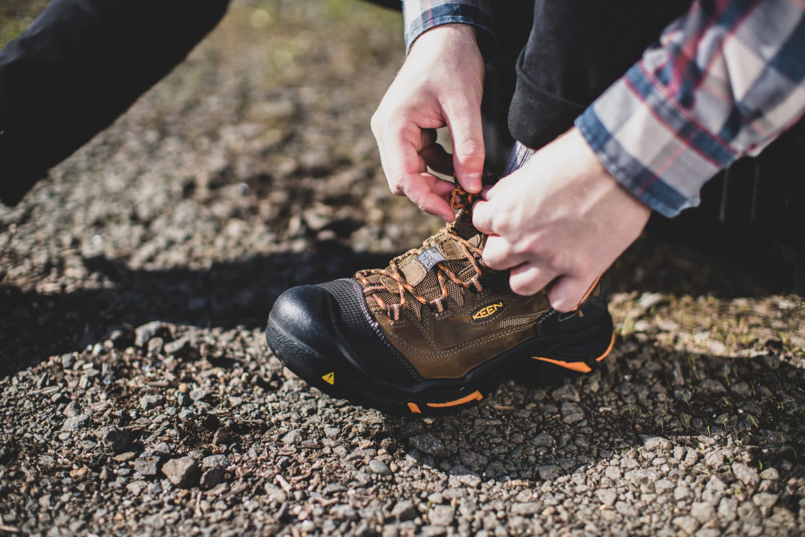 Hands lacing a work boot on gravel