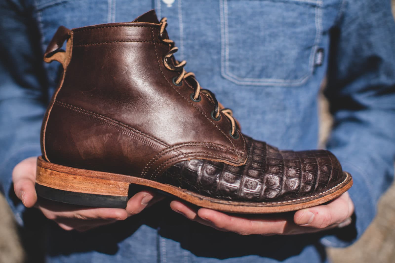 Hands presenting croc-embossed leather boot