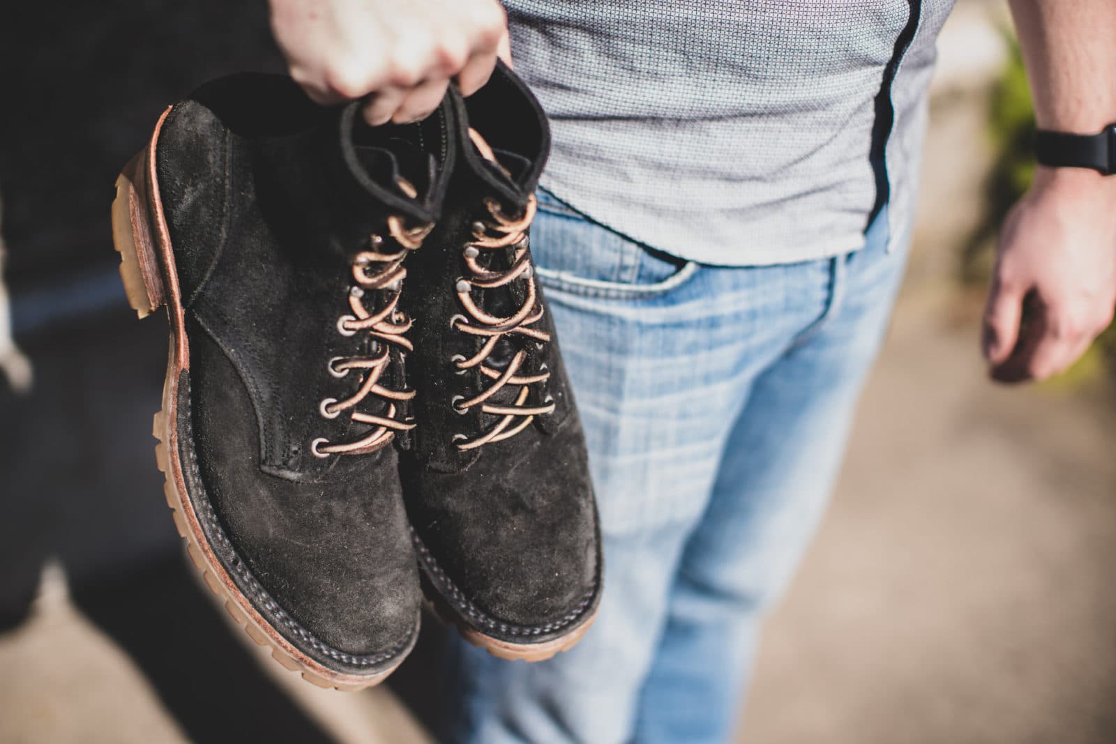 Man holding black suede boots by laces