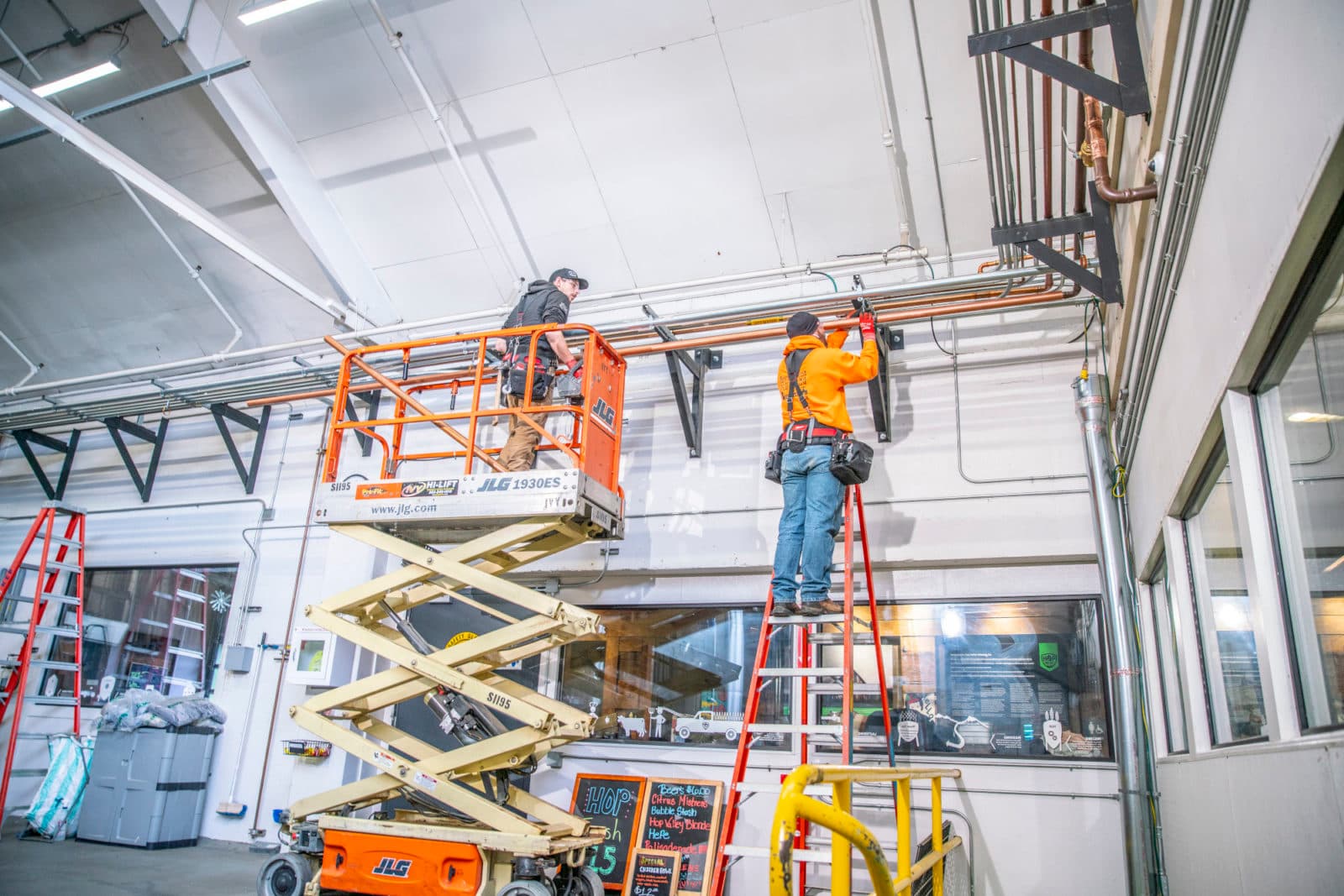 Workers on lift and ladder in bright brewery
