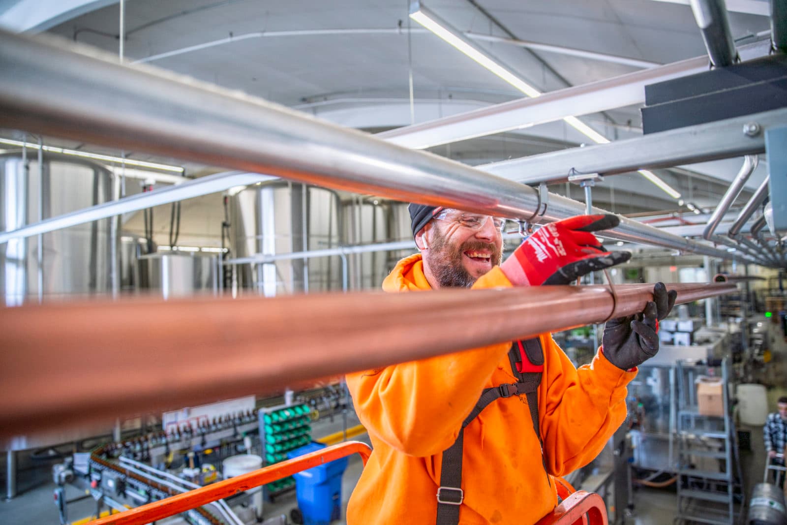 Smiling plumber with copper pipe in brewery