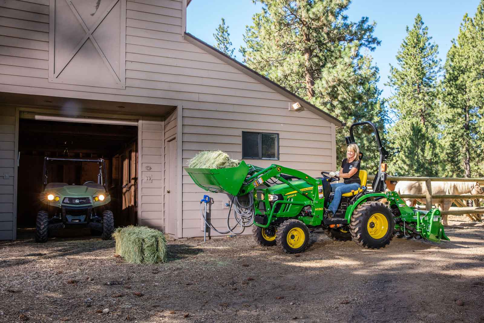 John Deere compact tractor carrying hay at barn