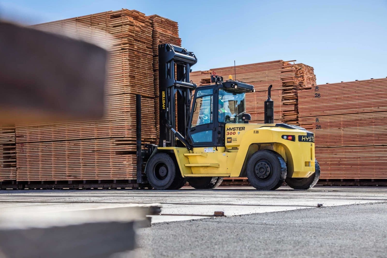 Forklift beside tall lumber stacks, blue sky