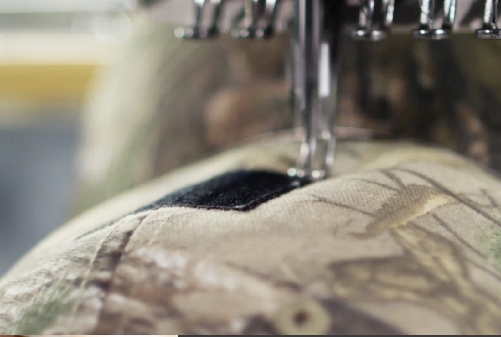 An embroidery needle stitching a logo onto a camouflage cap