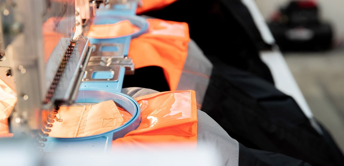 Embroidery hoops holding orange garments on FPW’s machines